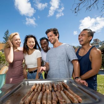 Students having BBQ at the beach cooking sausages